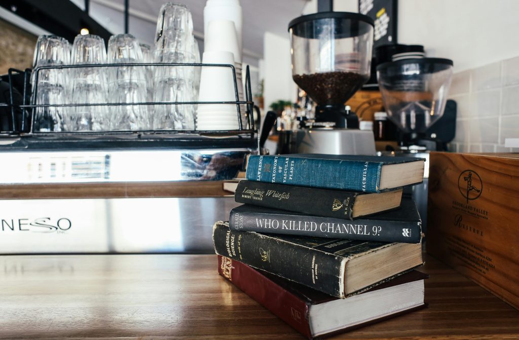 Stack of books beside coffee grinder and glassware in a cozy café setting.